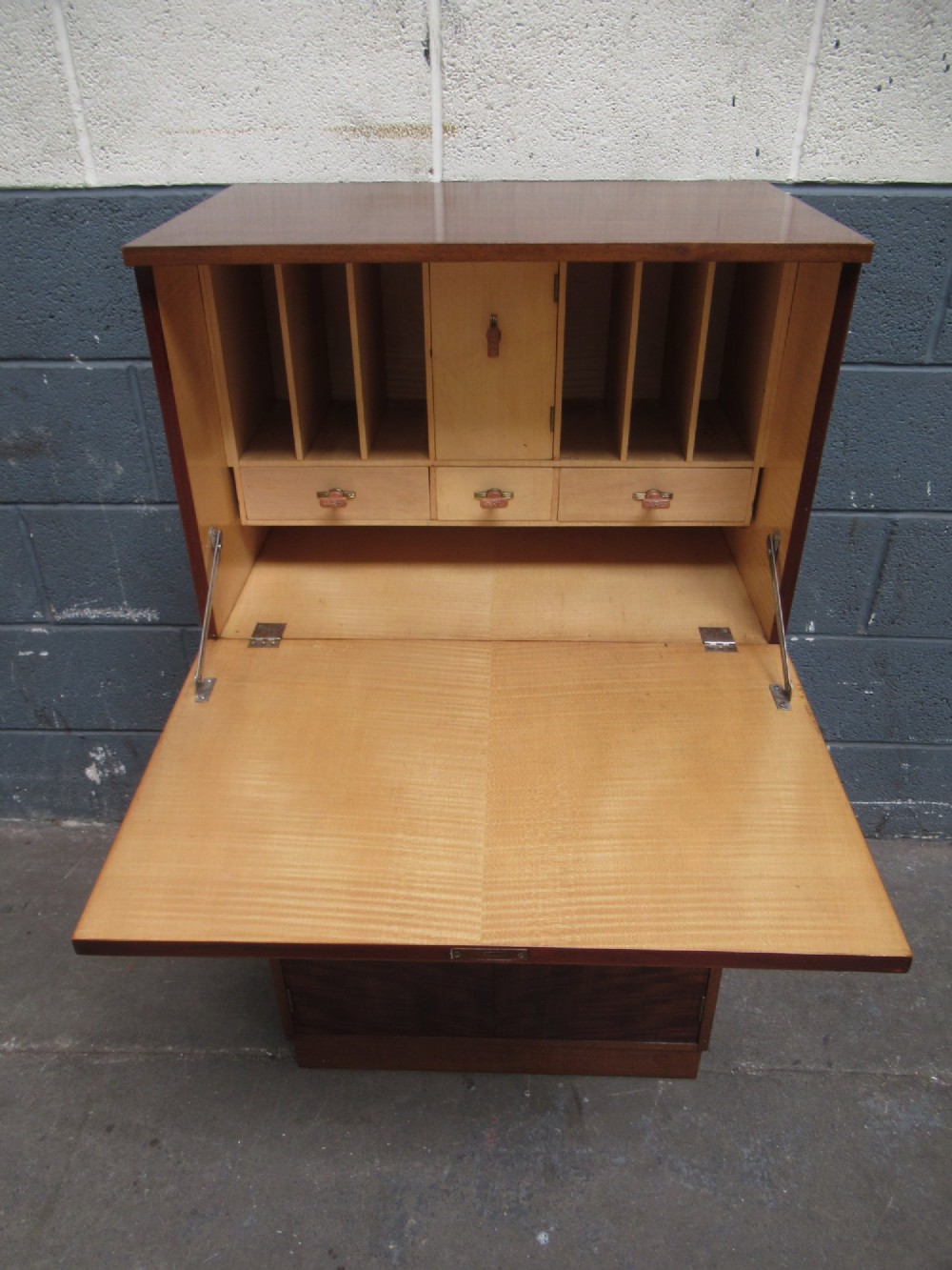 An Art Deco writing bureau in dark brown veneered wood featuring an open fall-front flap that reveals a light-coloured fitted interior with drawers and pigeonholes. View II