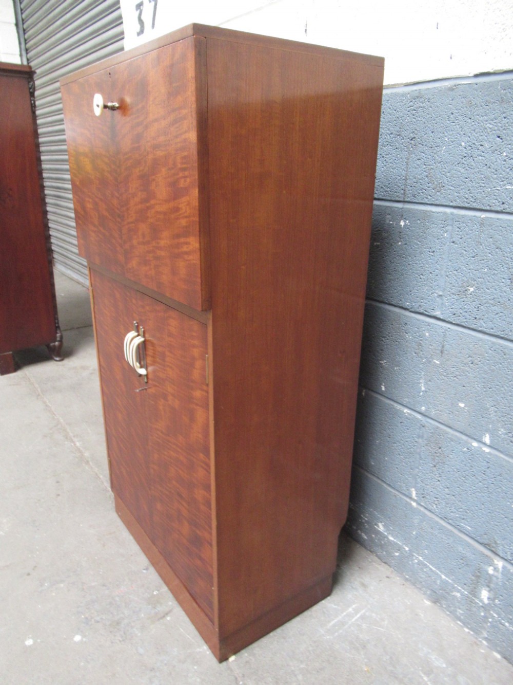 An Art Deco writing bureau in dark brown veneered wood featuring an open fall-front flap that reveals a light-coloured fitted interior with drawers and pigeonholes. View VII