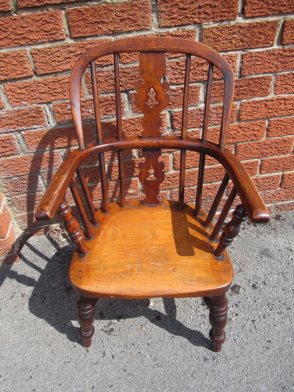 A warm brown wooden childs Windsor armchair with a hoop back, central pierced splat, turned legs, and a solid shaped seat.