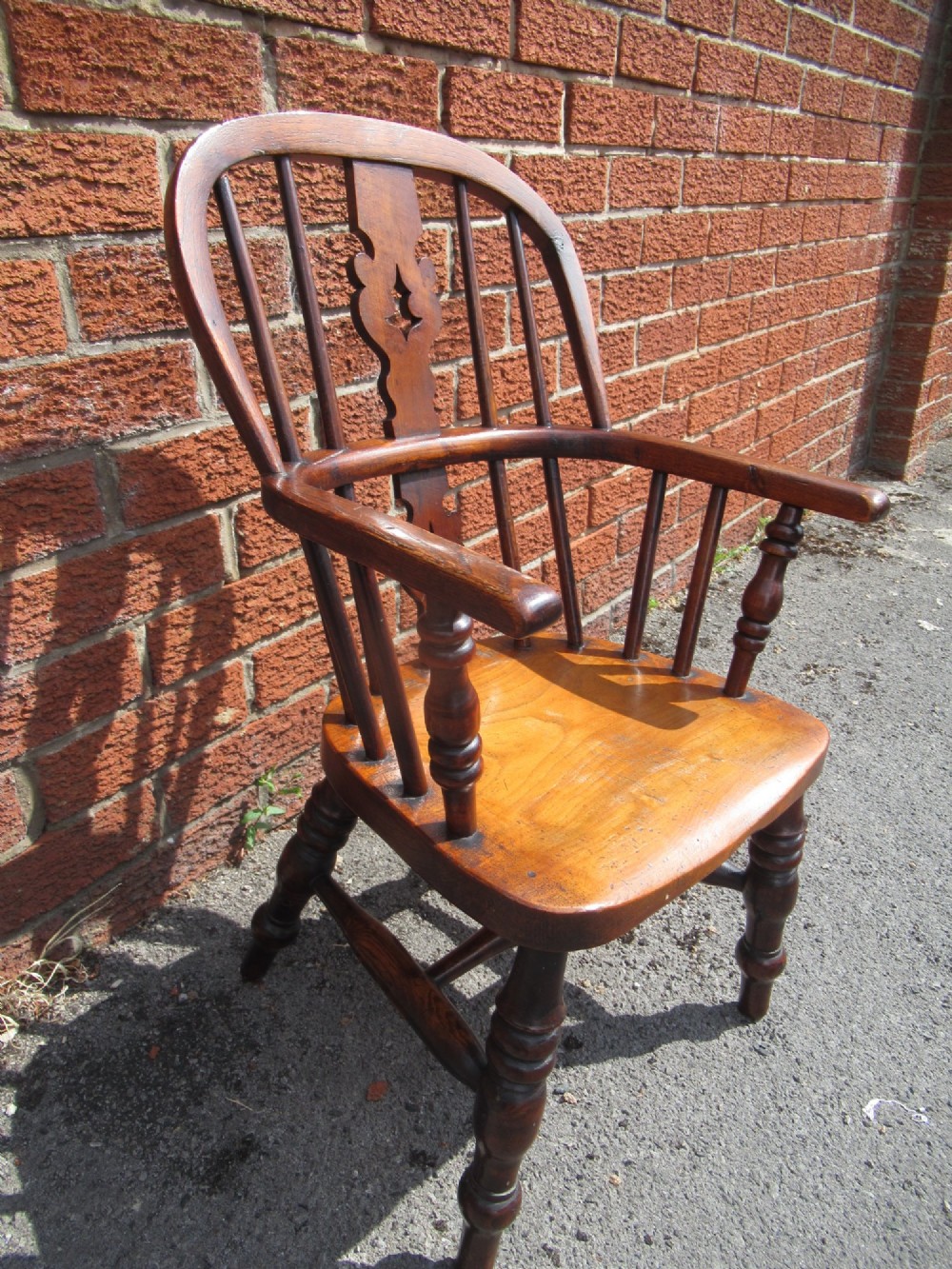 A warm brown wooden childs Windsor armchair with a hoop back, central pierced splat, turned legs, and a solid shaped seat. View II