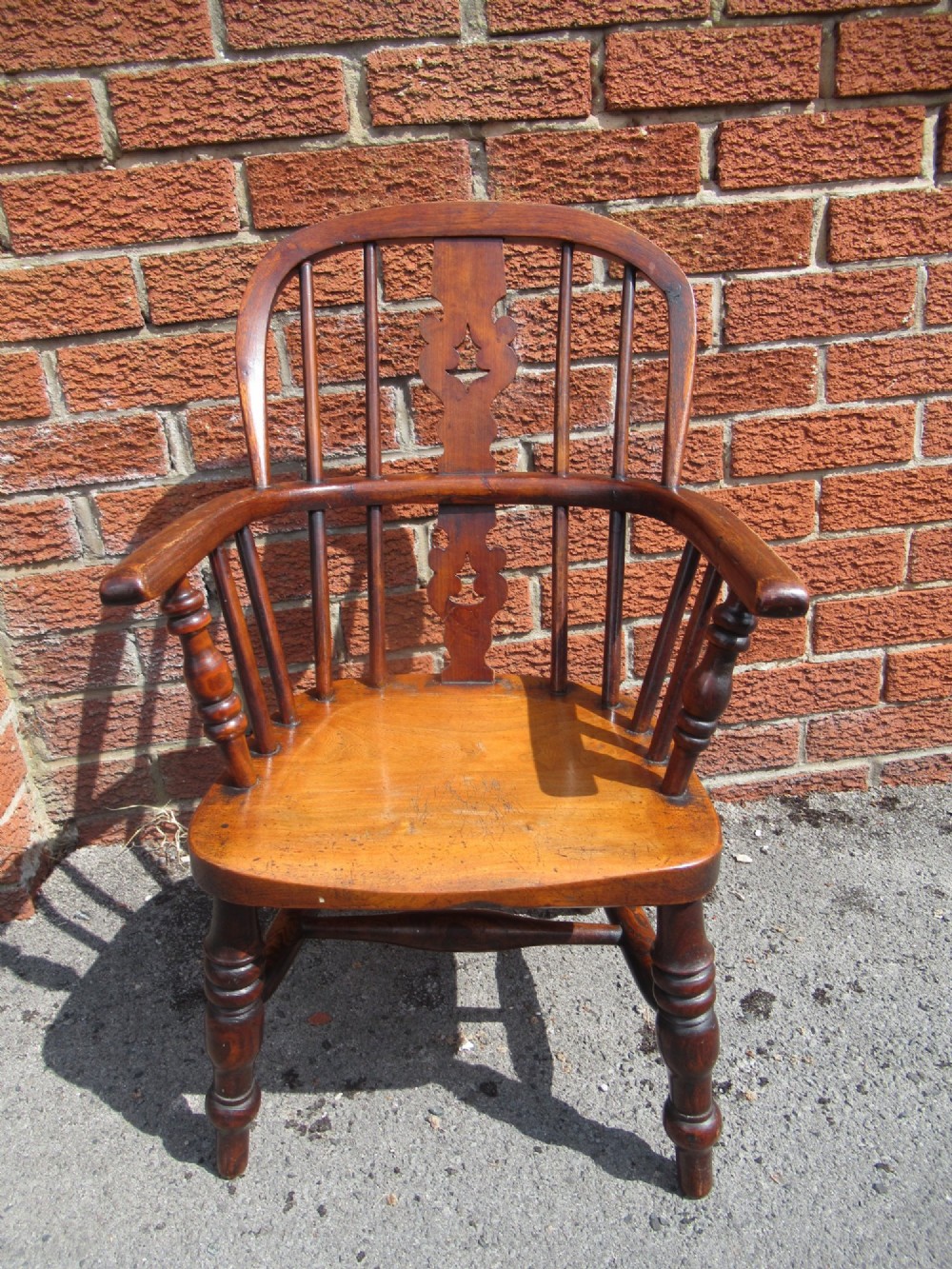 A warm brown wooden childs Windsor armchair with a hoop back, central pierced splat, turned legs, and a solid shaped seat. View III
