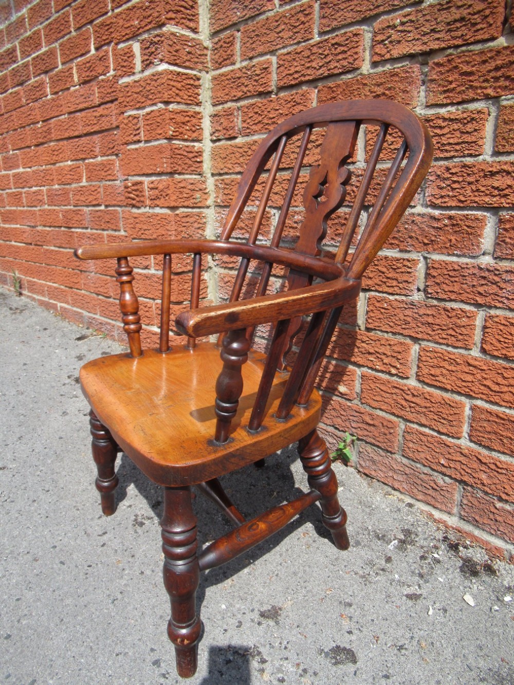 A warm brown wooden childs Windsor armchair with a hoop back, central pierced splat, turned legs, and a solid shaped seat. View IV