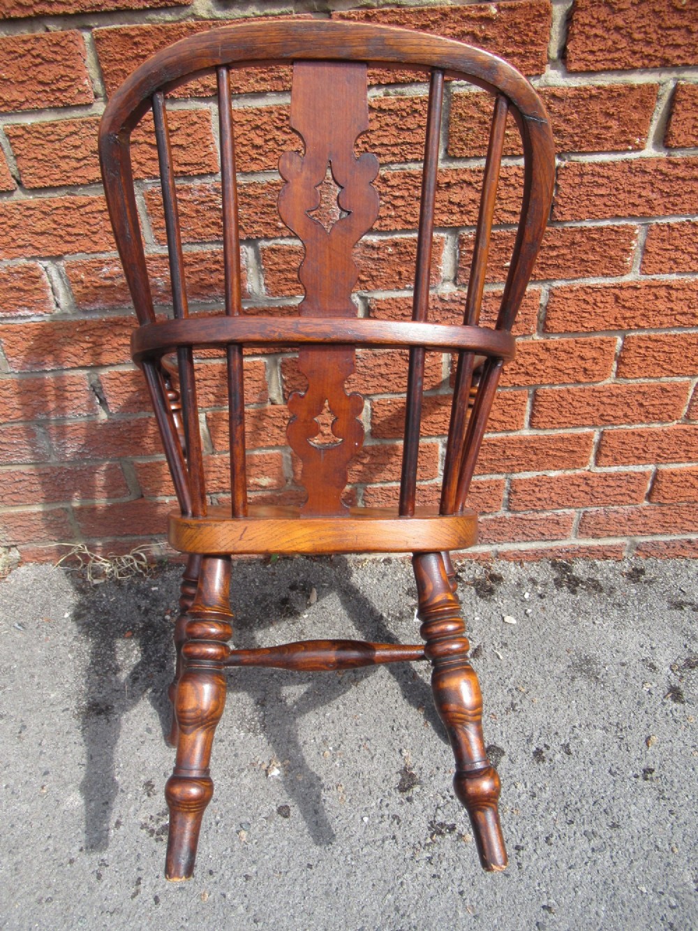 A warm brown wooden childs Windsor armchair with a hoop back, central pierced splat, turned legs, and a solid shaped seat. View VII