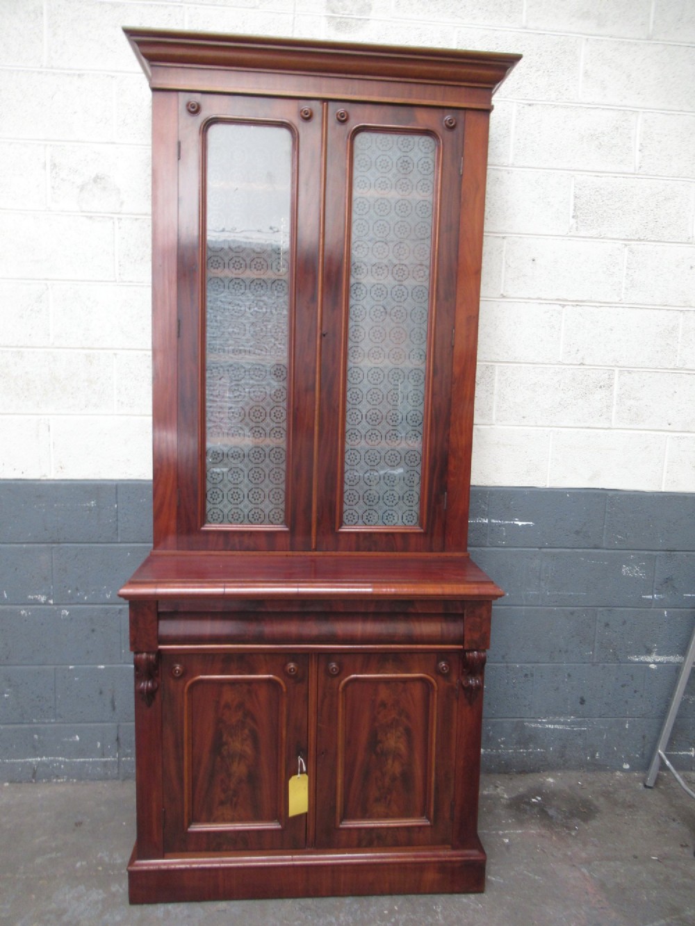 A tall 19th-century Victorian mahogany glazed bookcase featuring a two-door upper section above a lower cupboard base with carved corbels.