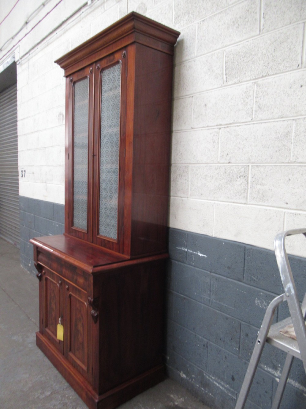 A tall 19th-century Victorian mahogany glazed bookcase featuring a two-door upper section above a lower cupboard base with carved corbels. View IV