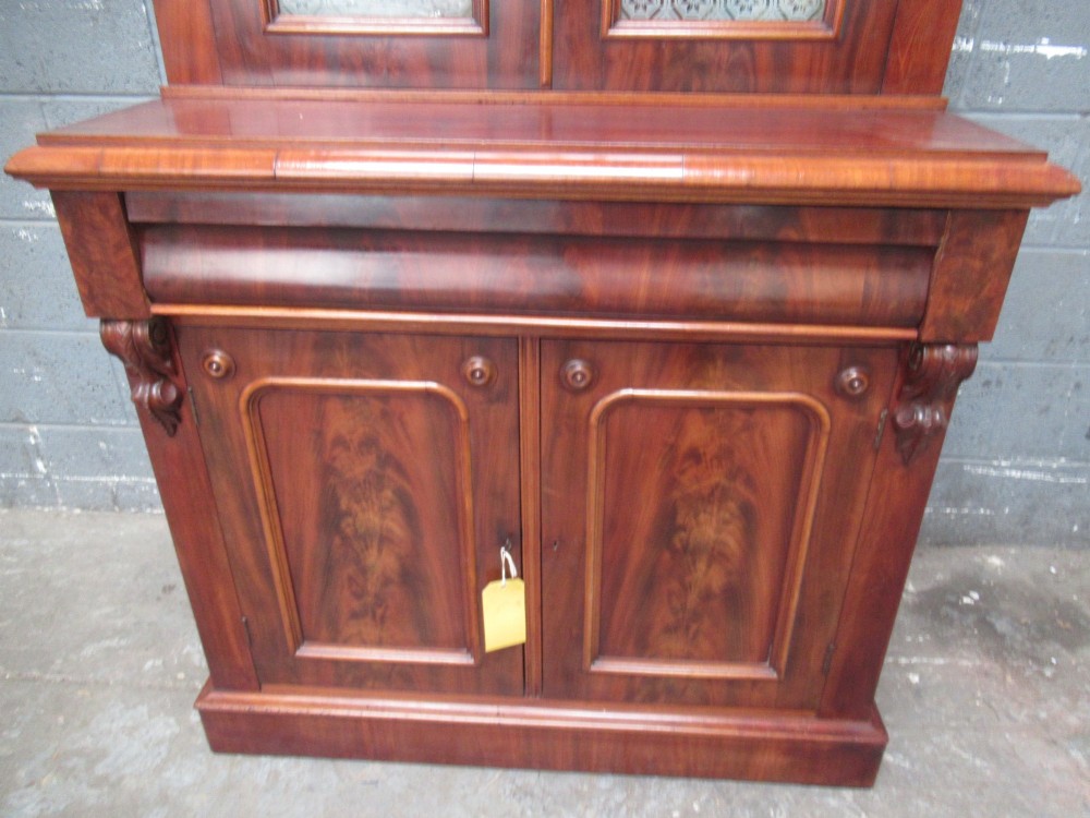 A tall 19th-century Victorian mahogany glazed bookcase featuring a two-door upper section above a lower cupboard base with carved corbels. View V