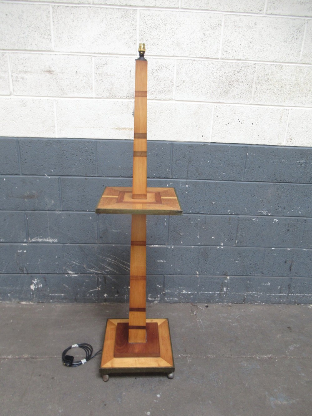 An Art Deco floor lamp crafted from geometric timber marquetry, featuring a central square tray table, a tall square column, and a stepped brass-rimmed base.