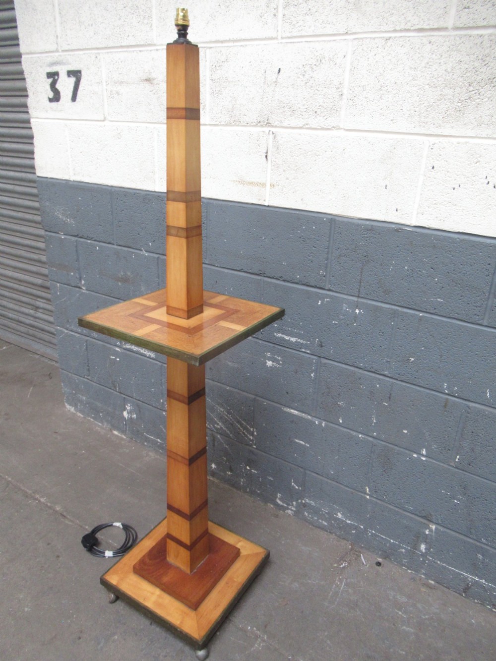 An Art Deco floor lamp crafted from geometric timber marquetry, featuring a central square tray table, a tall square column, and a stepped brass-rimmed base. View IX