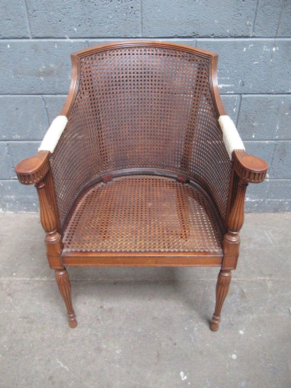 A mahogany tub-shaped armchair featuring a continuous woven cane backrest and seat with fluted front legs. View II