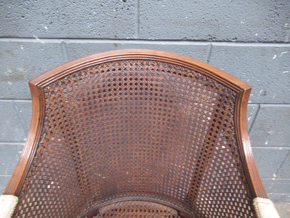 A mahogany tub-shaped armchair featuring a continuous woven cane backrest and seat with fluted front legs. View V