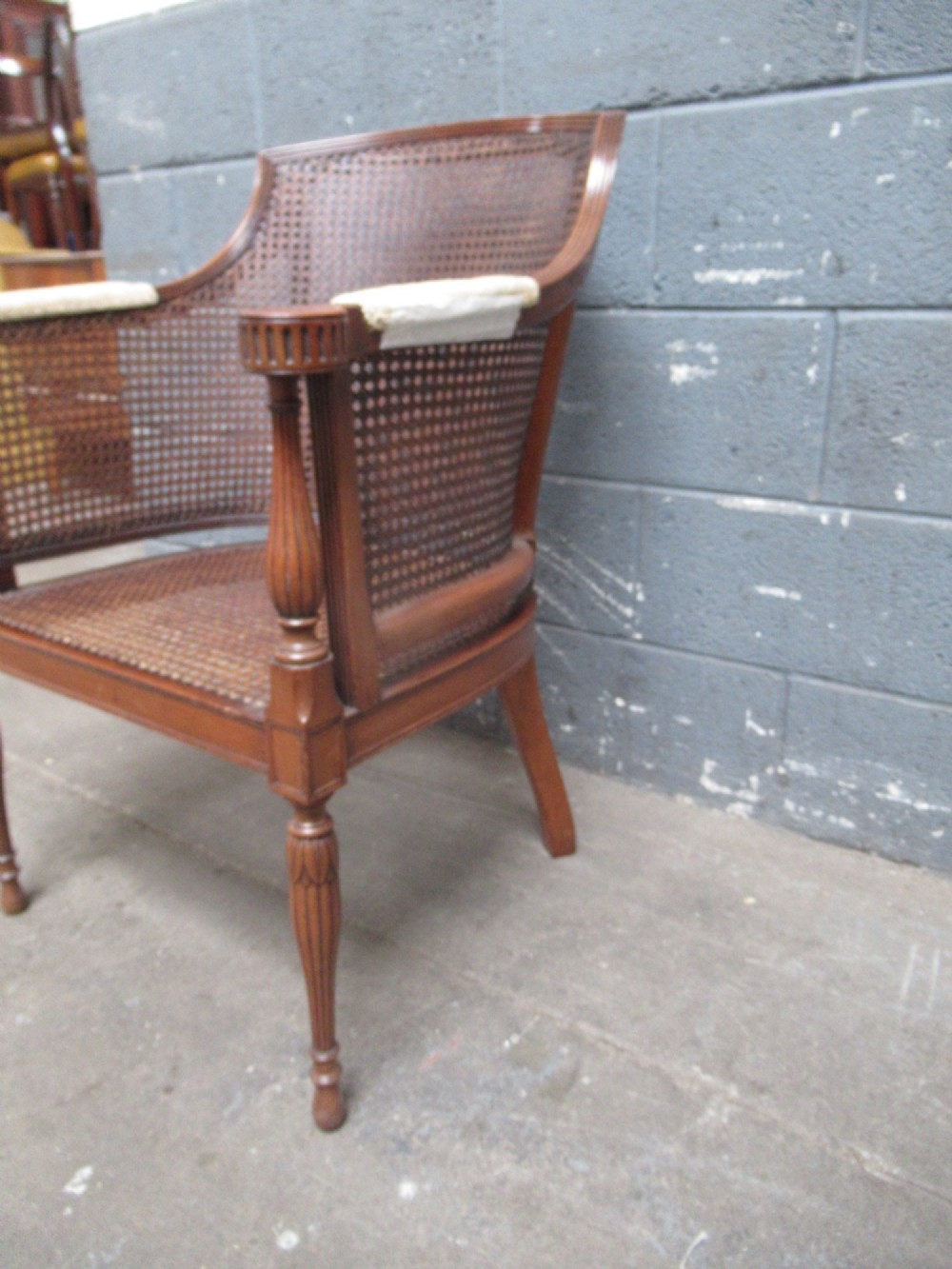 A mahogany tub-shaped armchair featuring a continuous woven cane backrest and seat with fluted front legs. View VII