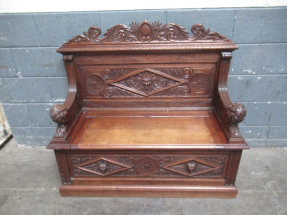 A late Victorian carved oak bench seat featuring relief grotesque masks, geometric lozenge panels, scrollwork cresting, and lion head armrest terminations. View II