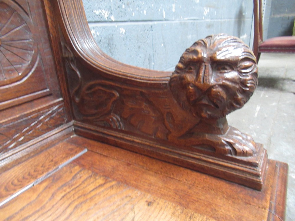 A late Victorian carved oak bench seat featuring relief grotesque masks, geometric lozenge panels, scrollwork cresting, and lion head armrest terminations. View V