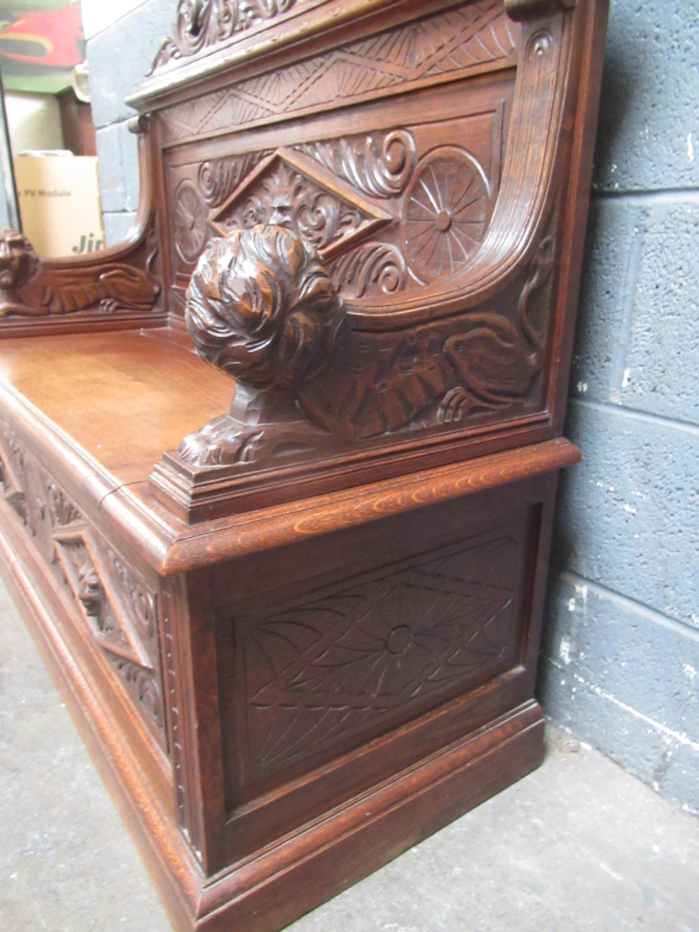 A late Victorian carved oak bench seat featuring relief grotesque masks, geometric lozenge panels, scrollwork cresting, and lion head armrest terminations. View VI