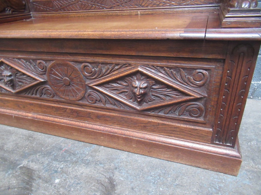 A late Victorian carved oak bench seat featuring relief grotesque masks, geometric lozenge panels, scrollwork cresting, and lion head armrest terminations. View VII