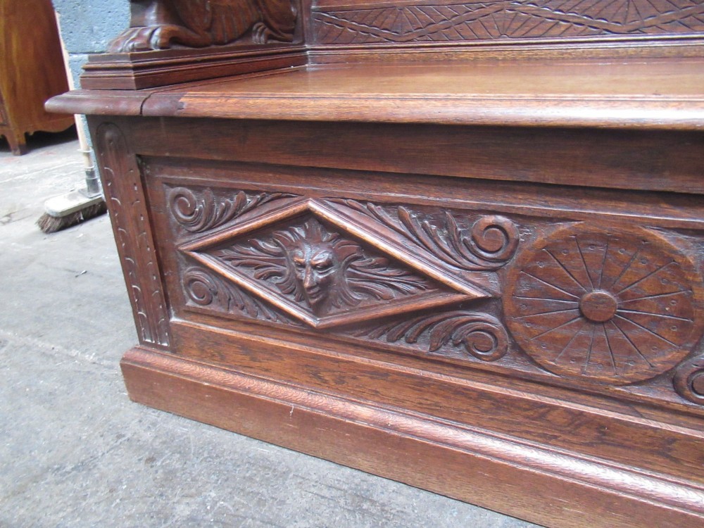 A late Victorian carved oak bench seat featuring relief grotesque masks, geometric lozenge panels, scrollwork cresting, and lion head armrest terminations. View VIII
