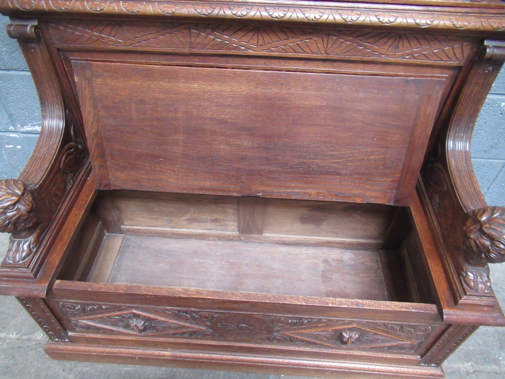 A late Victorian carved oak bench seat featuring relief grotesque masks, geometric lozenge panels, scrollwork cresting, and lion head armrest terminations. View IX