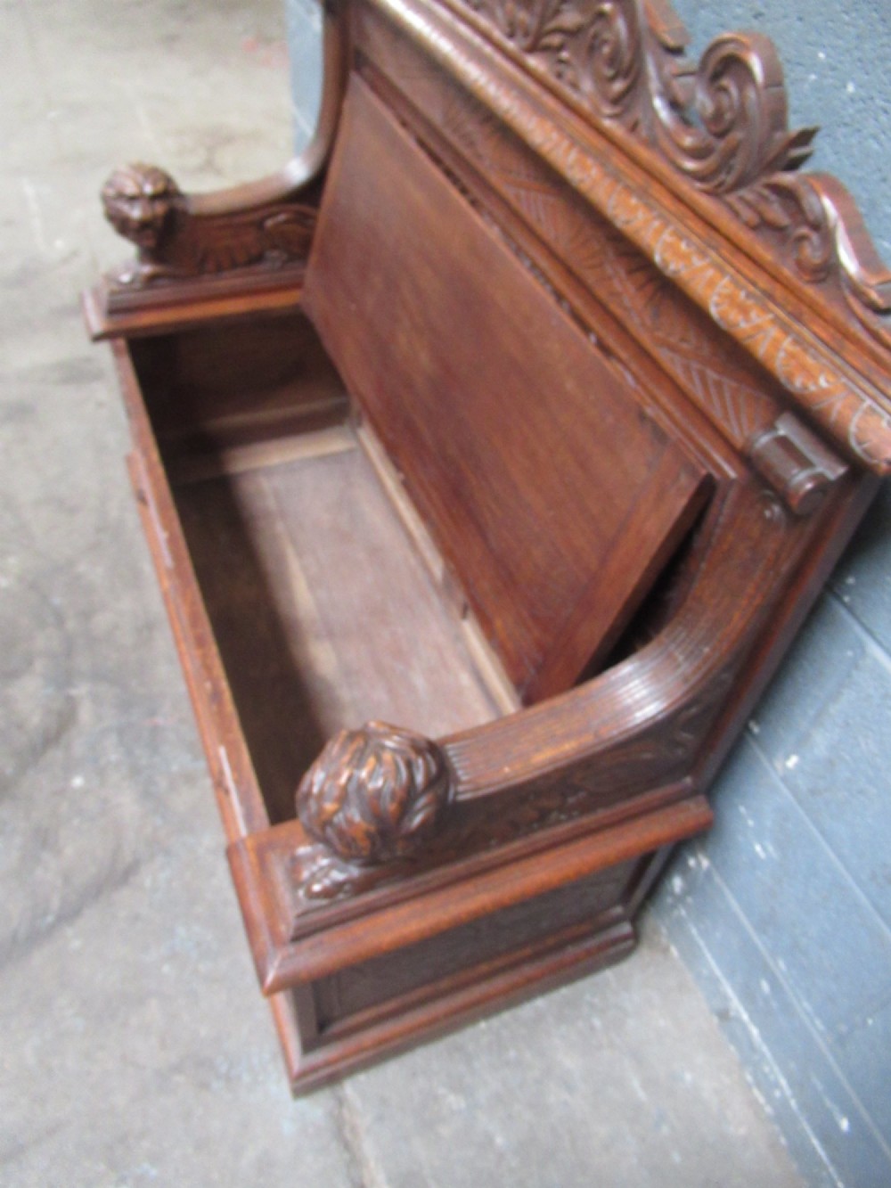 A late Victorian carved oak bench seat featuring relief grotesque masks, geometric lozenge panels, scrollwork cresting, and lion head armrest terminations. View X