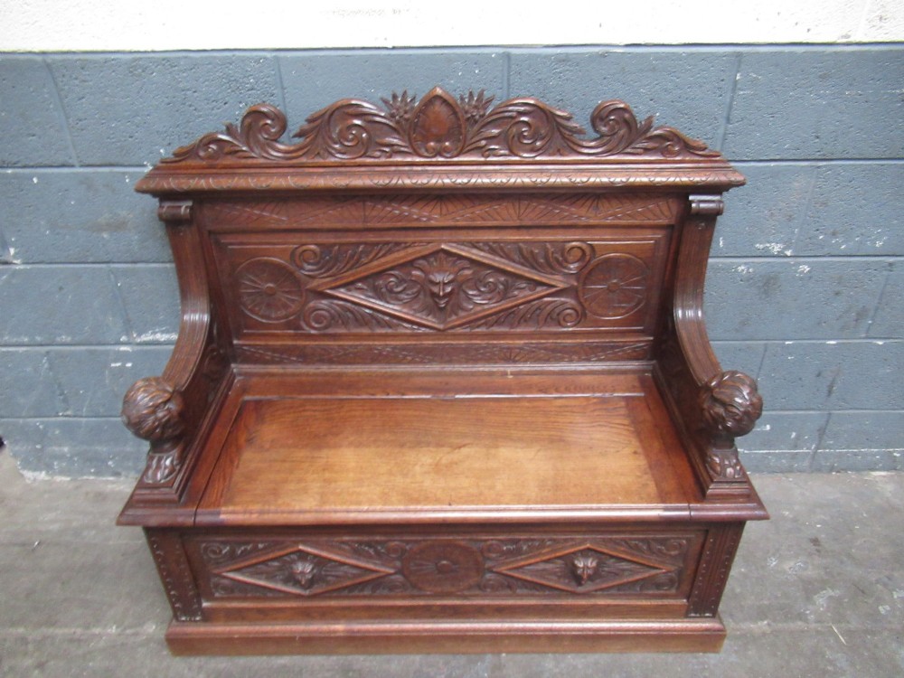 A late Victorian carved oak bench seat featuring relief grotesque masks, geometric lozenge panels, scrollwork cresting, and lion head armrest terminations. View XI