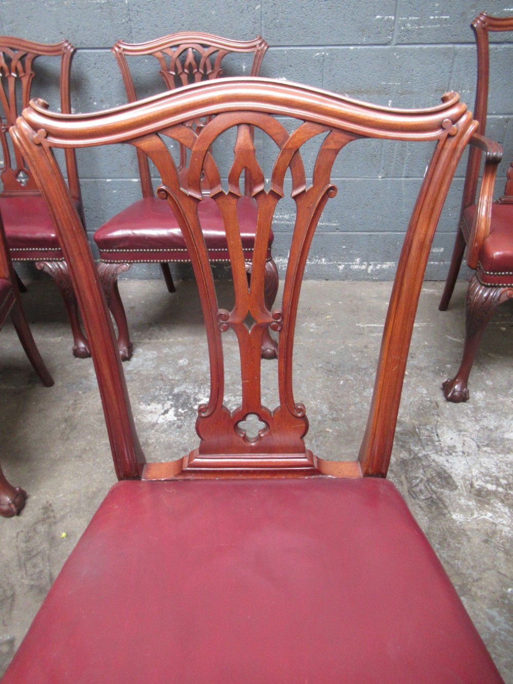 A set of eight mahogany Chippendale style dining chairs featuring carved pierced splats, red leather seats with brass studding, and cabriole legs with ball and claw feet. View VI