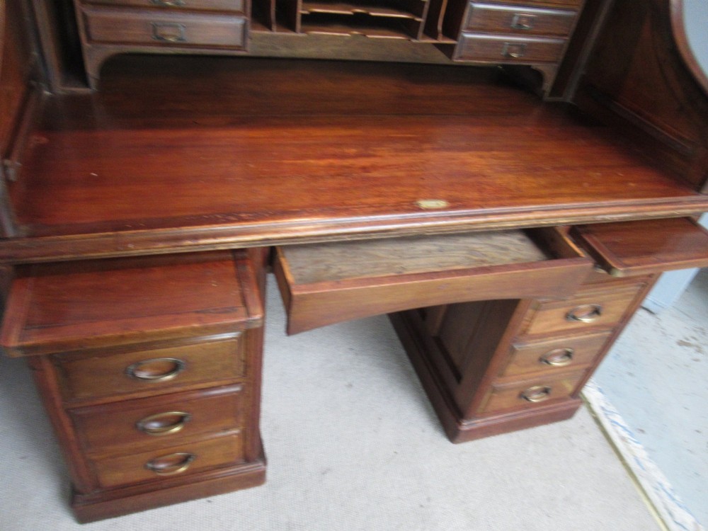 A large antique walnut roll-top desk featuring a slatted wooden tambour front over twin pedestals with eight brass-handled drawers. View VII