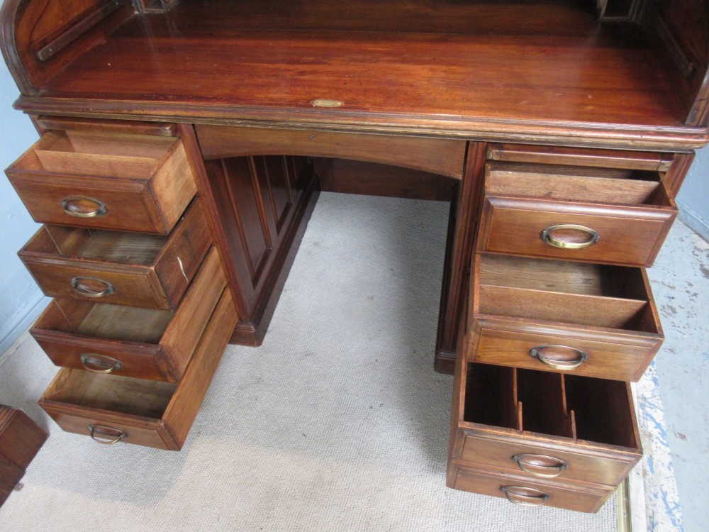 A large antique walnut roll-top desk featuring a slatted wooden tambour front over twin pedestals with eight brass-handled drawers. View VIII