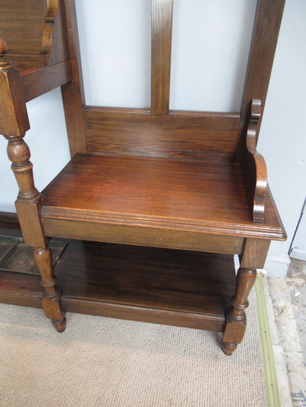 An Edwardian dark oak hall stand featuring an oval mirror, small glove drawer, integrated seat, stick holder, and multiple brass coat hooks. View III