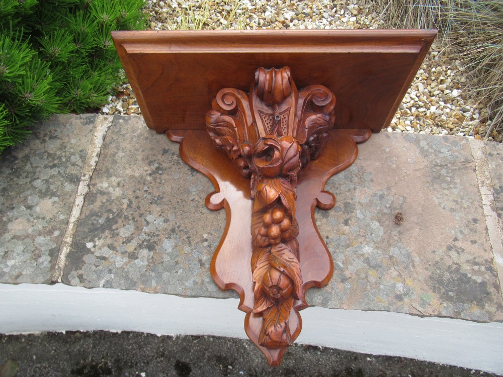 A carved Victorian walnut wall bracket featuring a flat top ledge supported by an ornate central motif of carved leaves, fruit, and scrollwork on a shaped backplate.