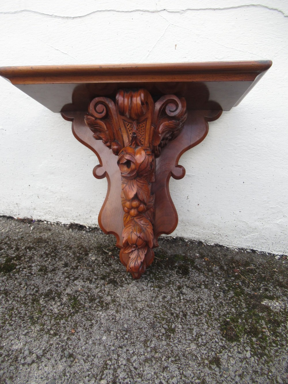 A carved Victorian walnut wall bracket featuring a flat top ledge supported by an ornate central motif of carved leaves, fruit, and scrollwork on a shaped backplate. View IV