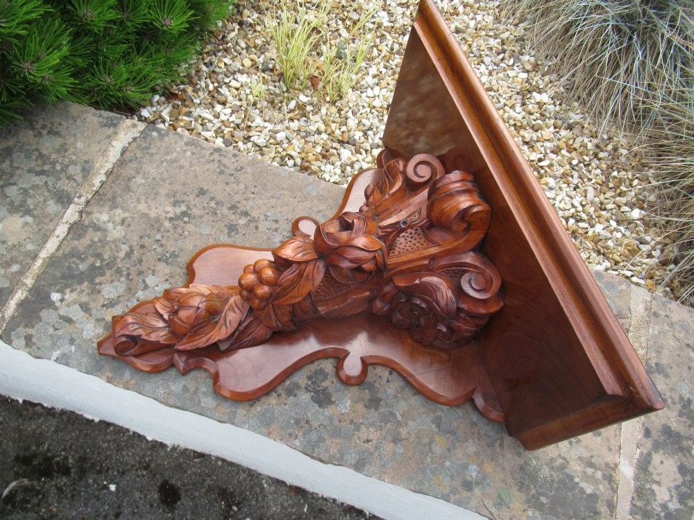 A carved Victorian walnut wall bracket featuring a flat top ledge supported by an ornate central motif of carved leaves, fruit, and scrollwork on a shaped backplate. View V