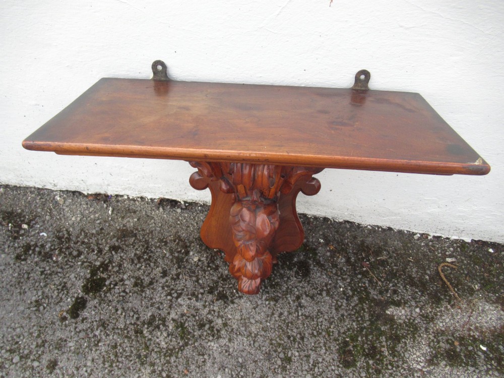 A carved Victorian walnut wall bracket featuring a flat top ledge supported by an ornate central motif of carved leaves, fruit, and scrollwork on a shaped backplate. View VI