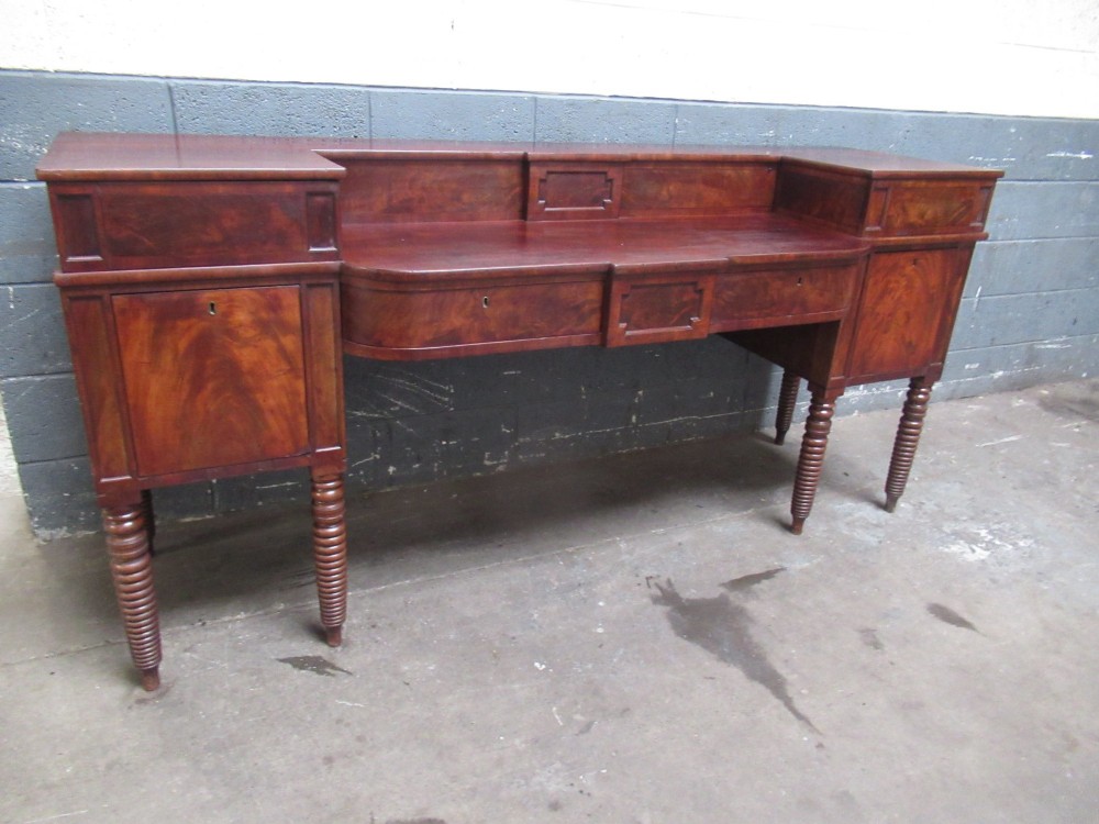 An early 19th century Scottish mahogany sideboard featuring a raised stage back, pedestal cupboards, central drawers, and spiral turned legs.