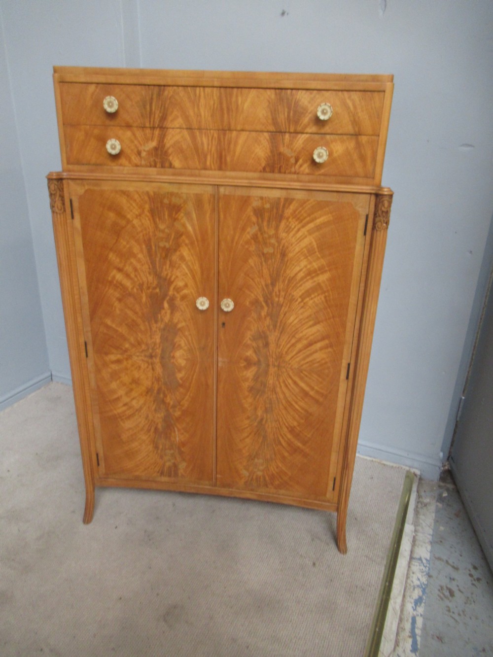 A mid-century fitted tallboy cabinet in pale mahogany and maple featuring two top drawers above double doors opening to reveal internal sliding shirt trays. View II