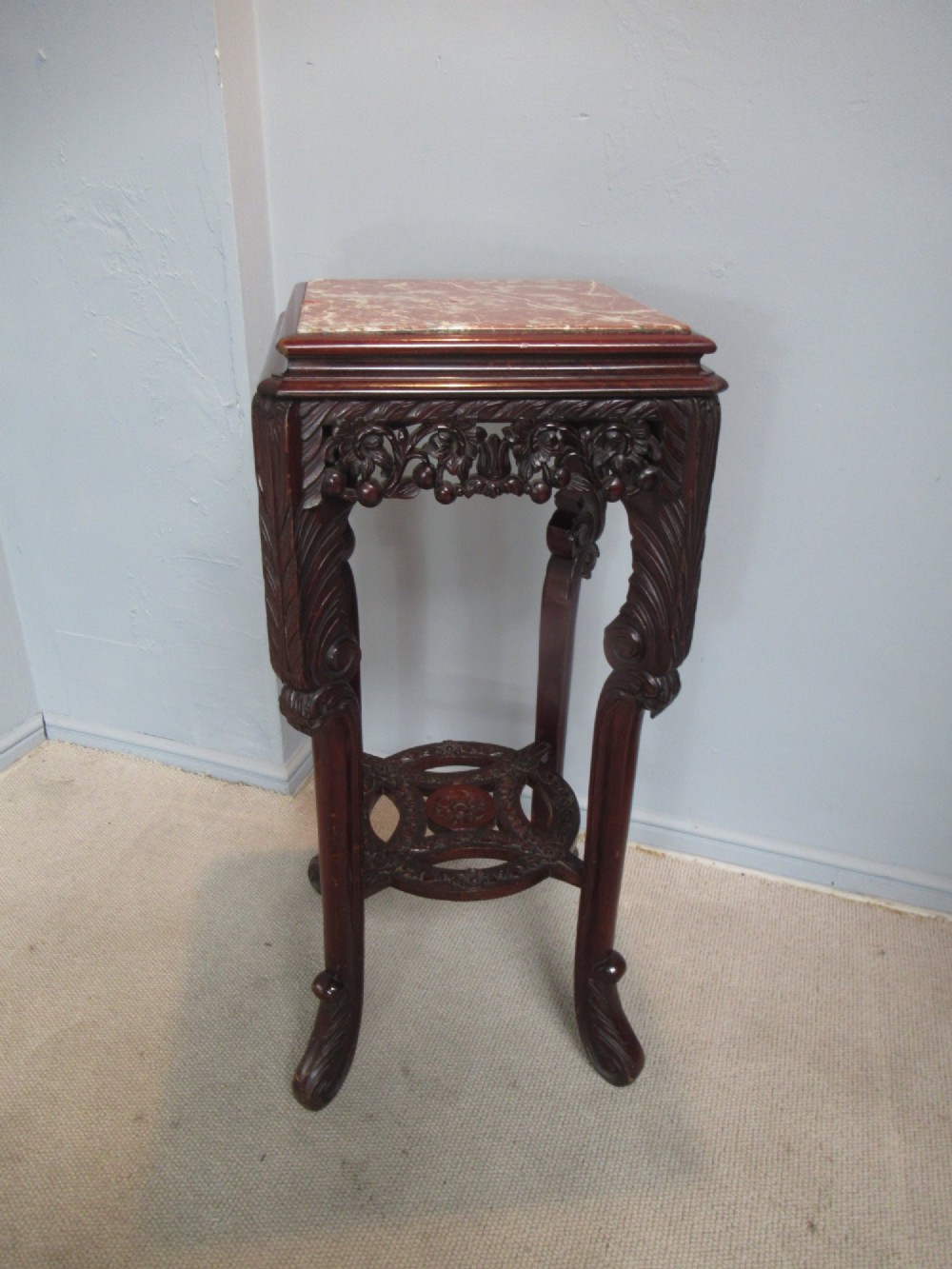 A tall carved dark hardwood stand featuring an inset rectangular pink marble top, ornate pierced apron, and a carved lower shelf. View IV