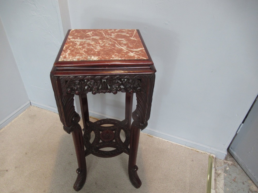 A tall carved dark hardwood stand featuring an inset rectangular pink marble top, ornate pierced apron, and a carved lower shelf. View V