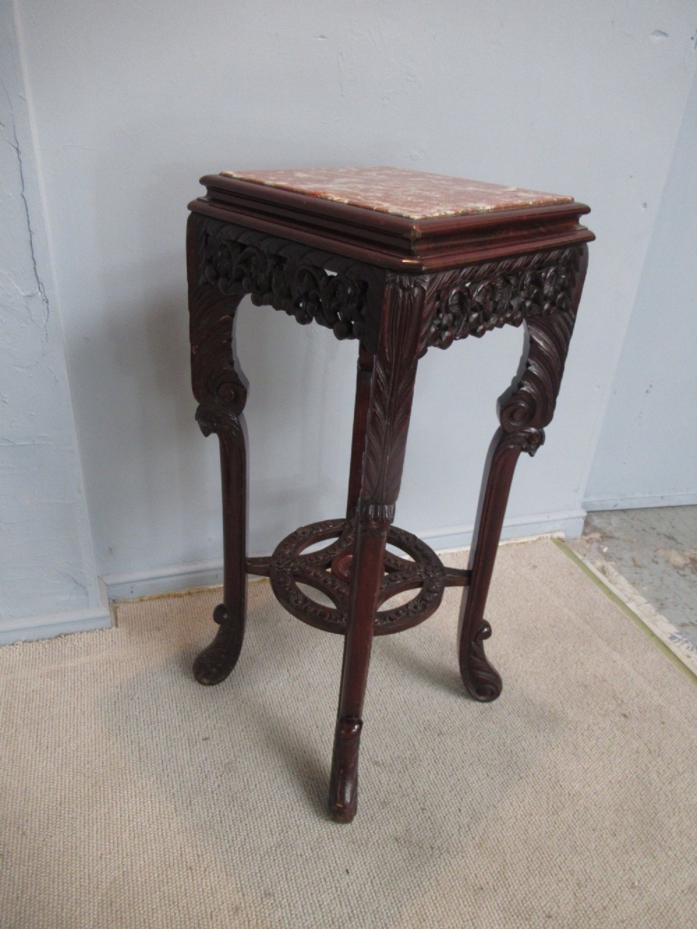 A tall carved dark hardwood stand featuring an inset rectangular pink marble top, ornate pierced apron, and a carved lower shelf. View VI