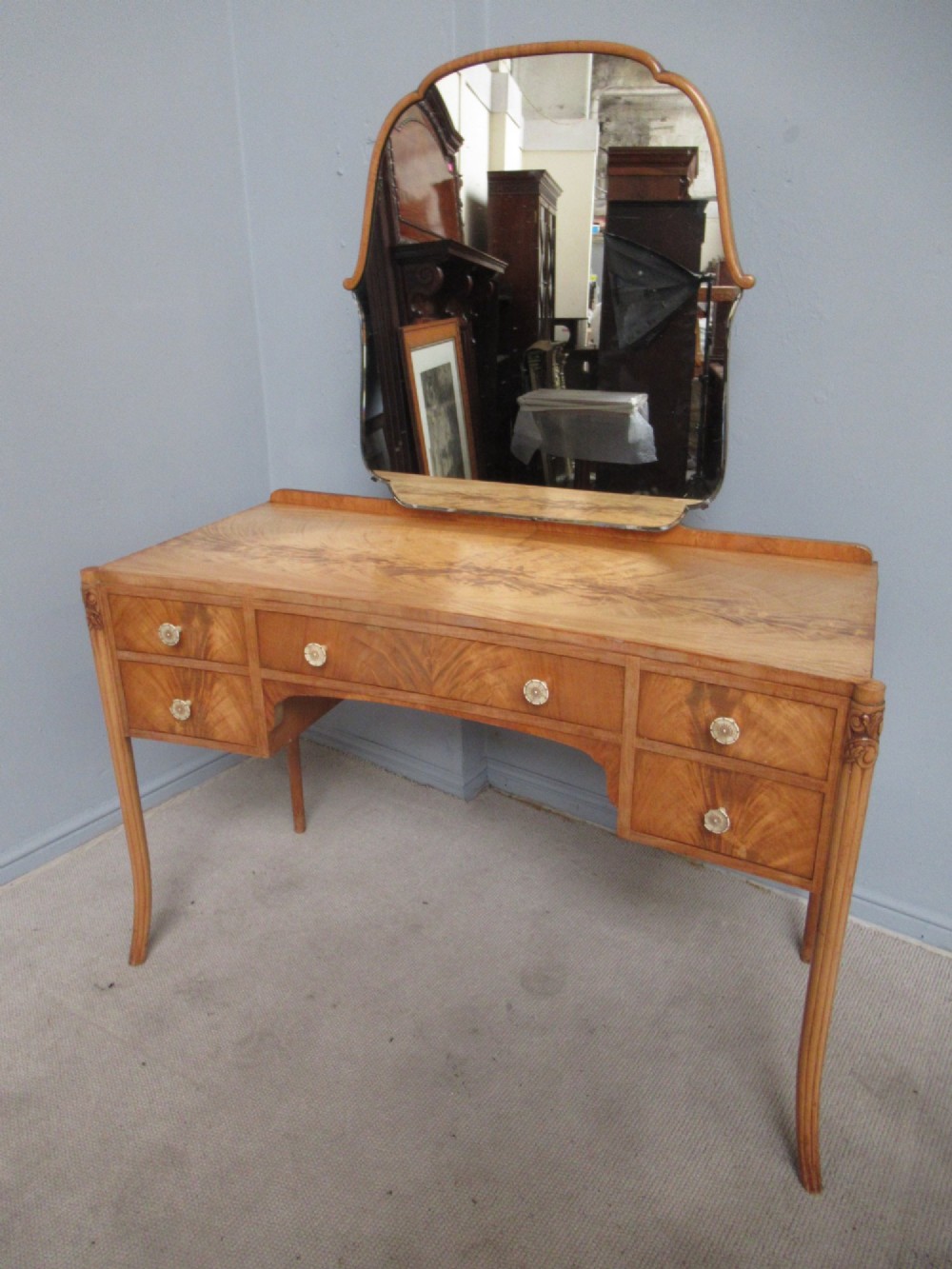 A 1930s Art Deco dressing table made from pale mahogany and maple, featuring an attached arched mirror, five drawers, and slender carved legs.