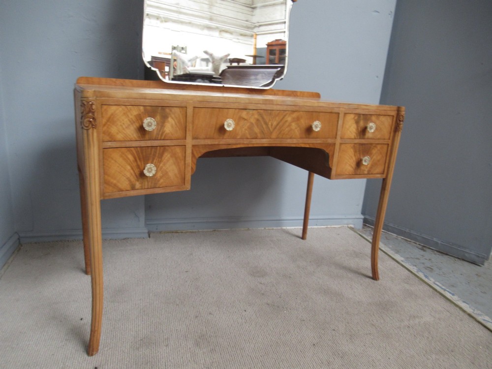 A 1930s Art Deco dressing table made from pale mahogany and maple, featuring an attached arched mirror, five drawers, and slender carved legs. View X
