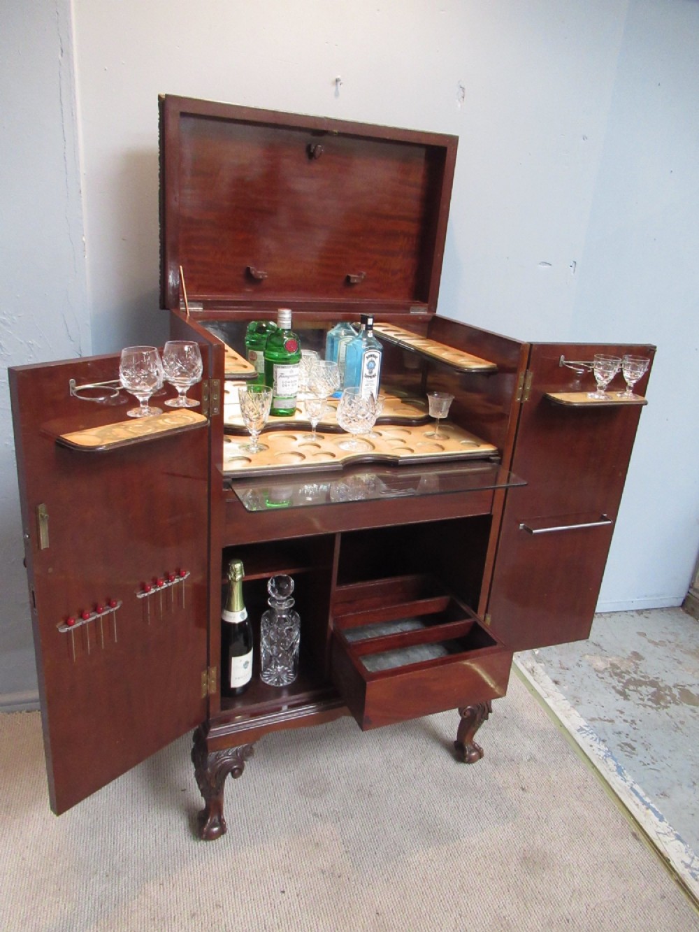 A mahogany Chippendale style cocktail cabinet shown open, revealing a mirrored interior, glass rack holders, and carved cabriole legs with ball-and-claw feet. View XII