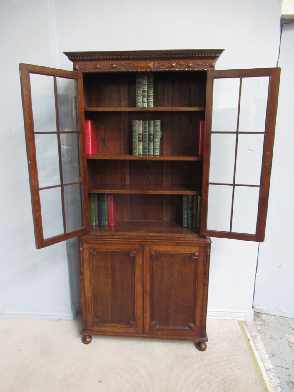 A tall 1920s dark oak bookcase featuring upper glazed doors with glass panes and a lower double-door cupboard base.