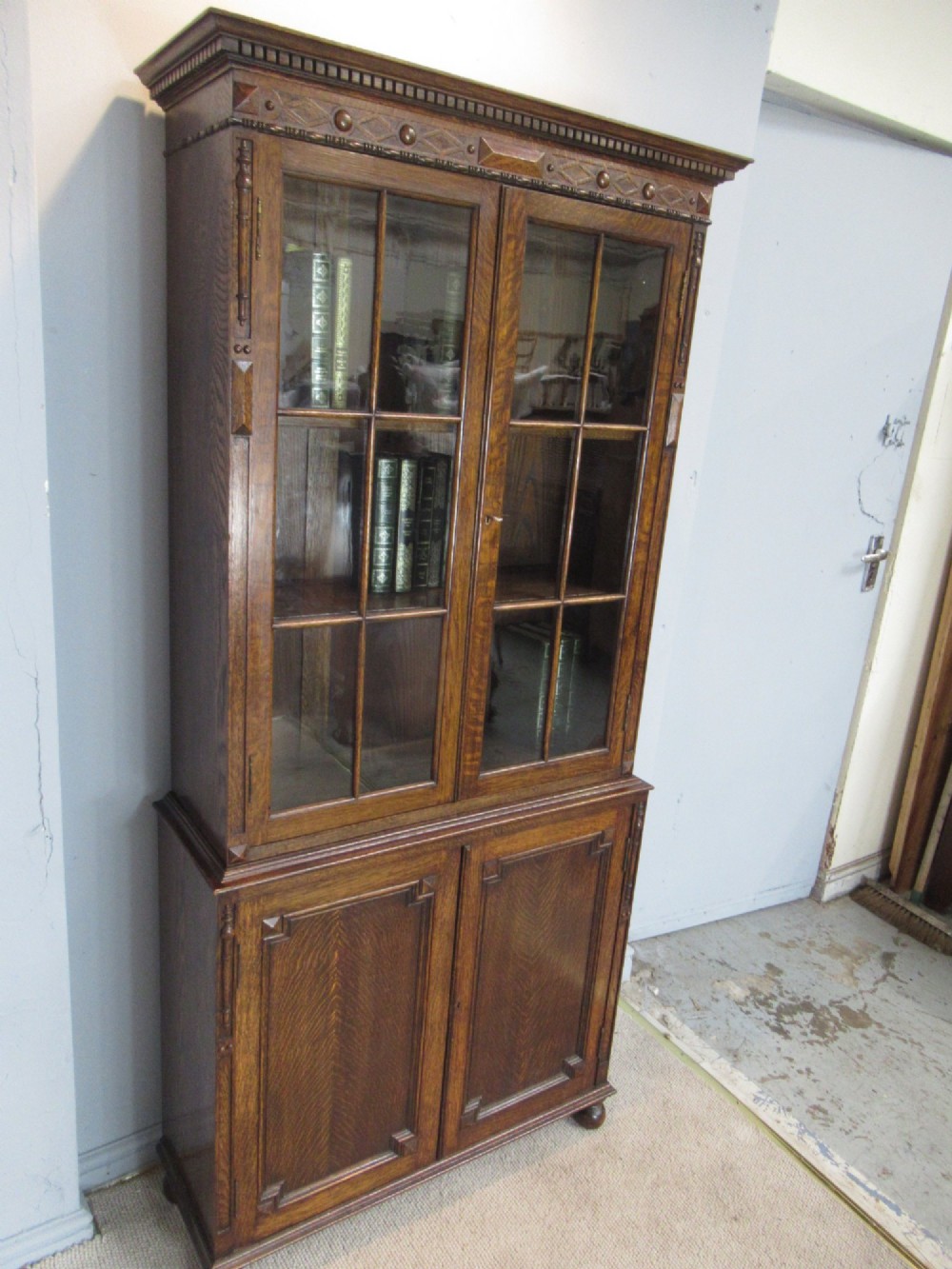 A tall 1920s dark oak bookcase featuring upper glazed doors with glass panes and a lower double-door cupboard base. View III
