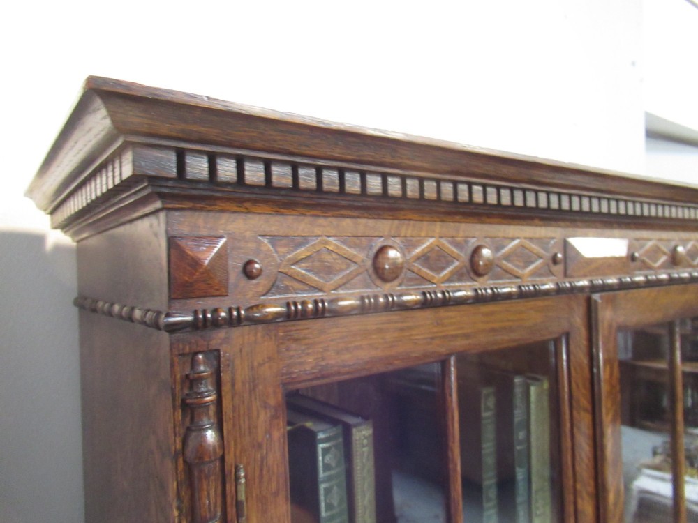 A tall 1920s dark oak bookcase featuring upper glazed doors with glass panes and a lower double-door cupboard base. View IV