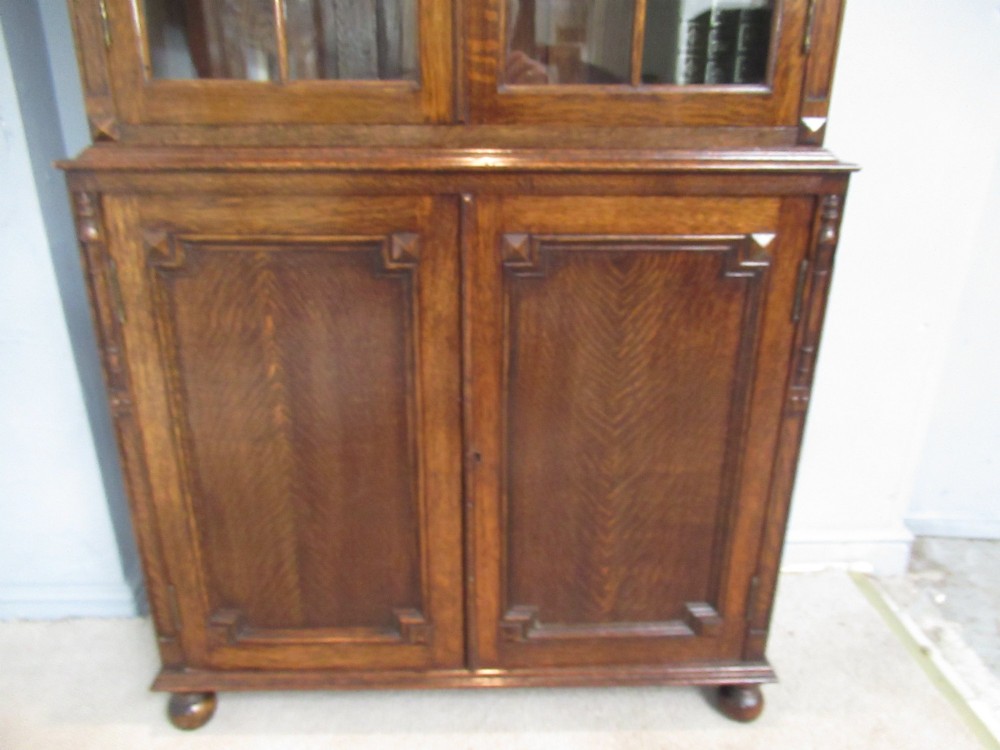A tall 1920s dark oak bookcase featuring upper glazed doors with glass panes and a lower double-door cupboard base. View V