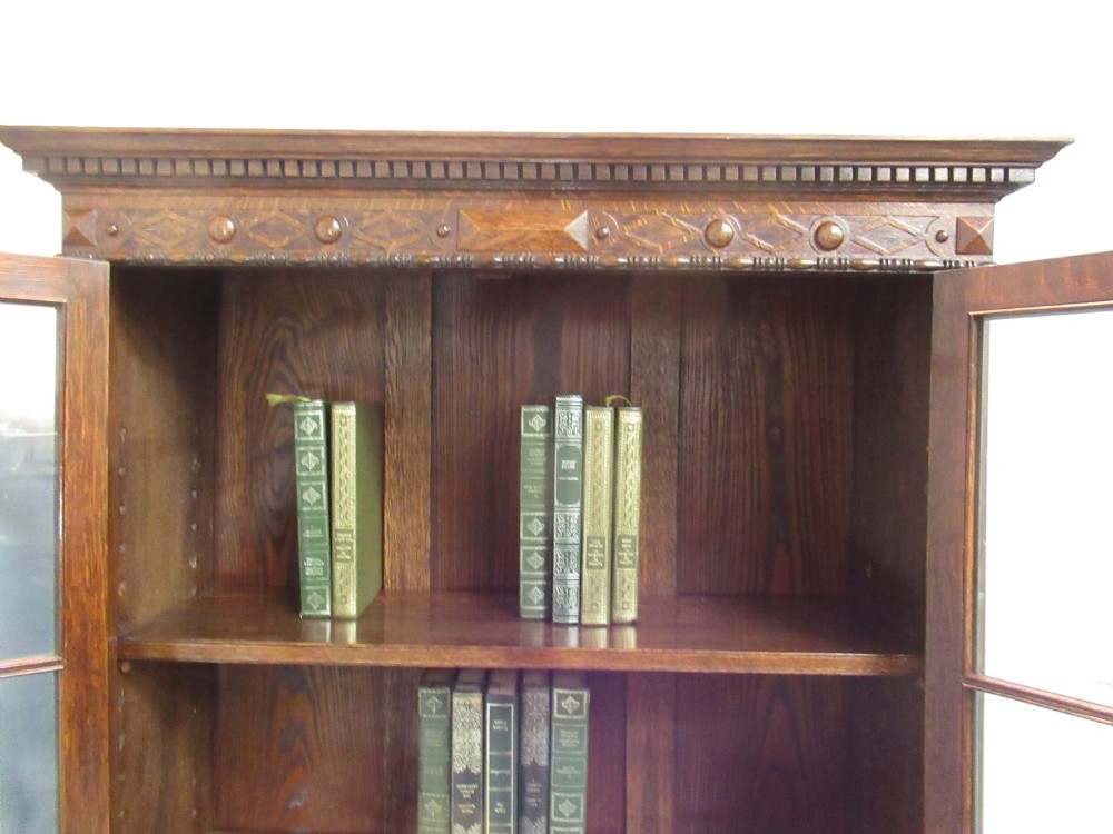 A tall 1920s dark oak bookcase featuring upper glazed doors with glass panes and a lower double-door cupboard base. View VI