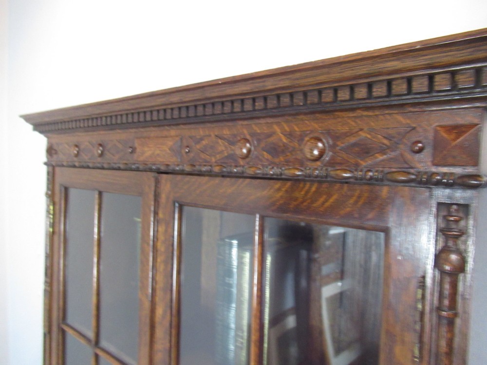 A tall 1920s dark oak bookcase featuring upper glazed doors with glass panes and a lower double-door cupboard base. View VII