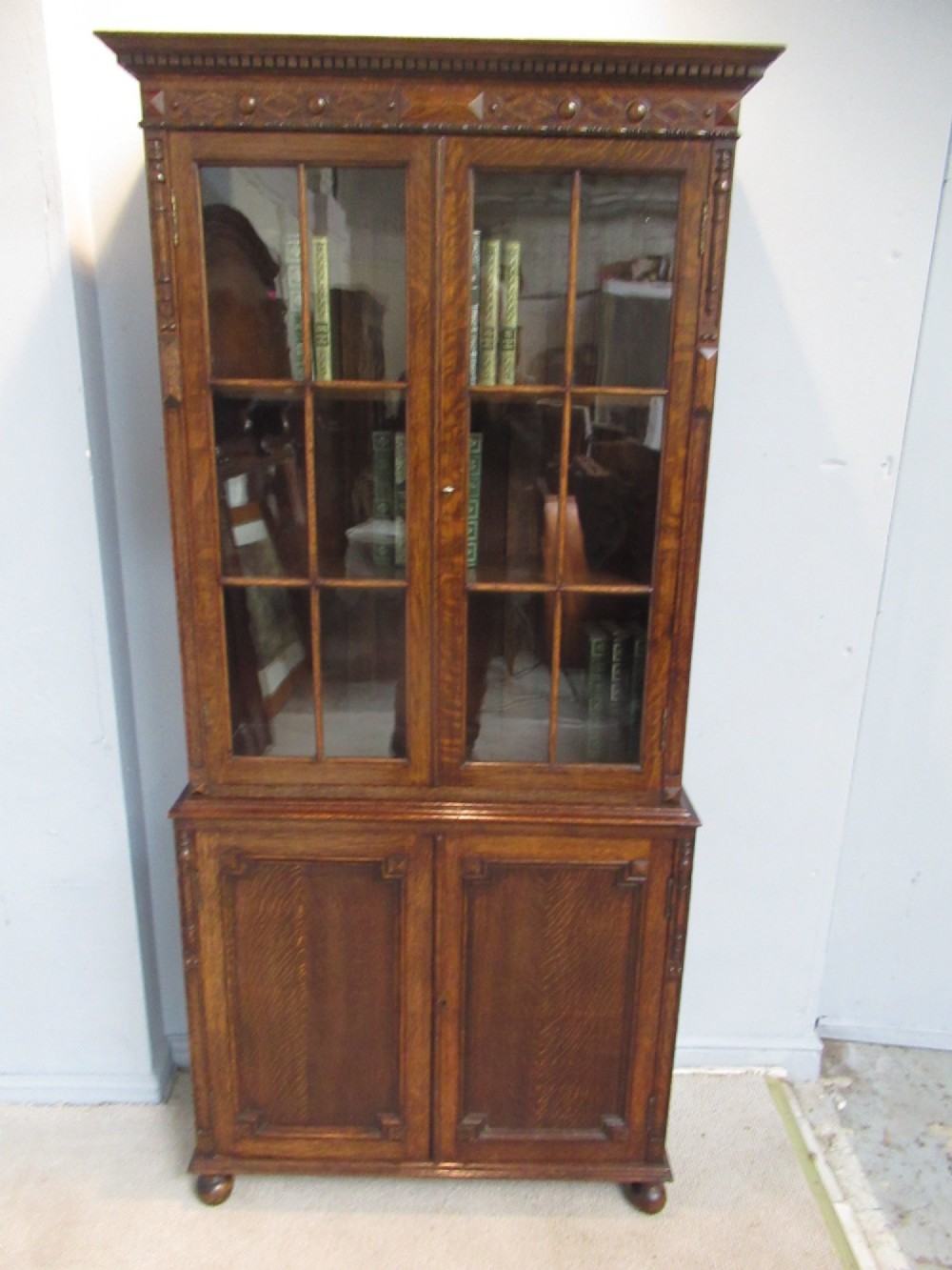 A tall 1920s dark oak bookcase featuring upper glazed doors with glass panes and a lower double-door cupboard base. View VIII