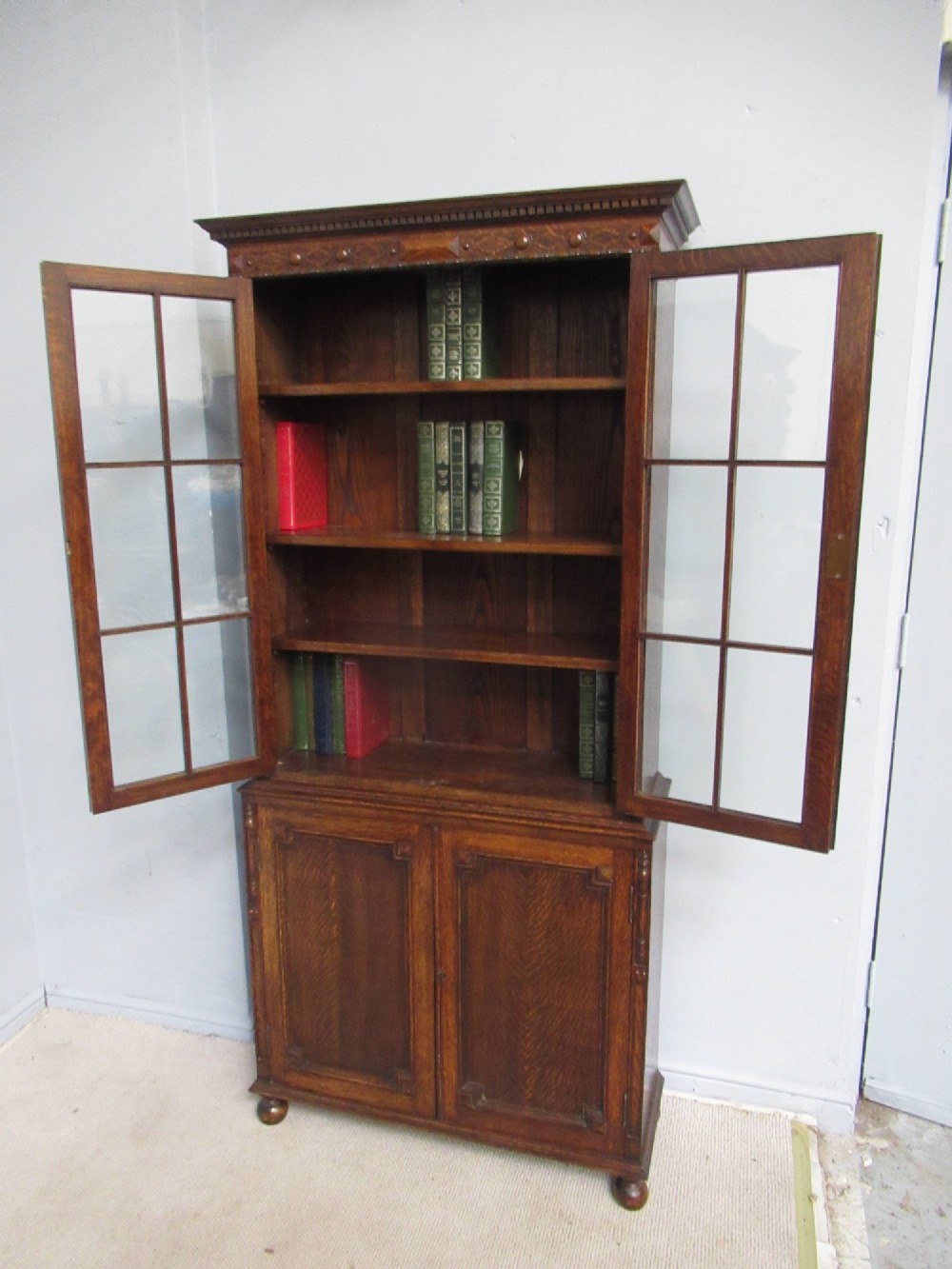 A tall 1920s dark oak bookcase featuring upper glazed doors with glass panes and a lower double-door cupboard base. View IX