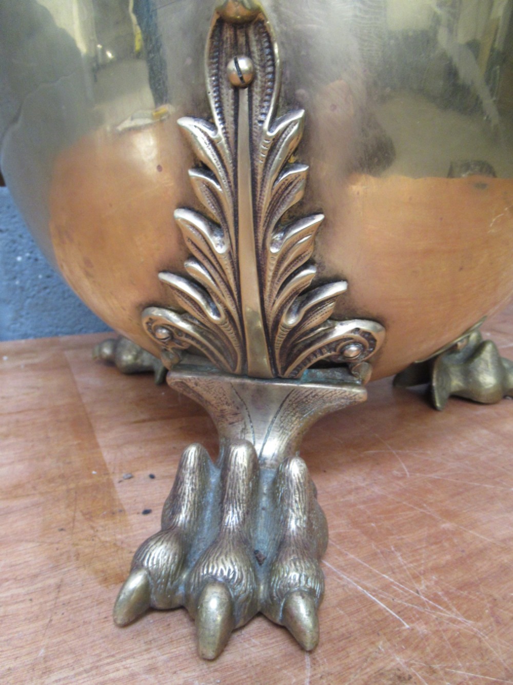 A polished brass lidded decorative bucket with a finial handle, lion mask side rings, and ornate claw feet. View VI