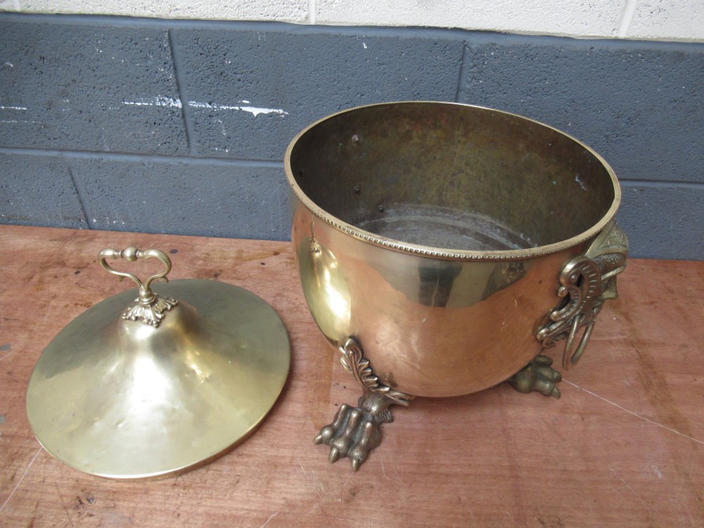 A polished brass lidded decorative bucket with a finial handle, lion mask side rings, and ornate claw feet. View VII