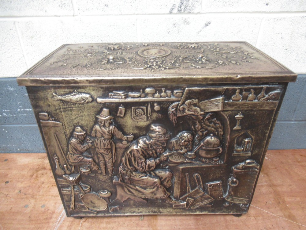A rectangular Victorian brass log box featuring a detailed embossed relief scene of figures inside a room on the front panel. View III